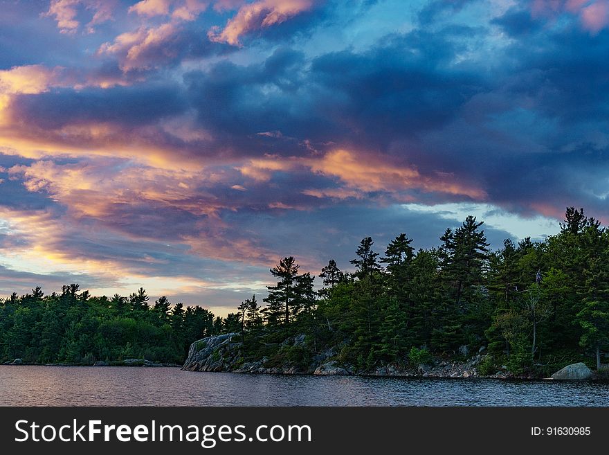 Scenic view of lake with forested coastline at dusk with dramatic cloudscape.