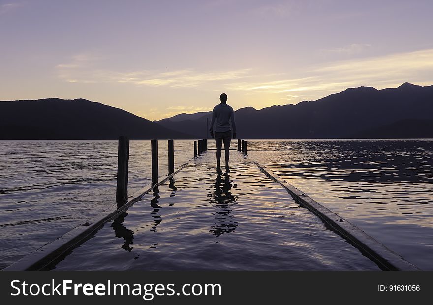 A person walking on a flooded pier at dusk. A person walking on a flooded pier at dusk.