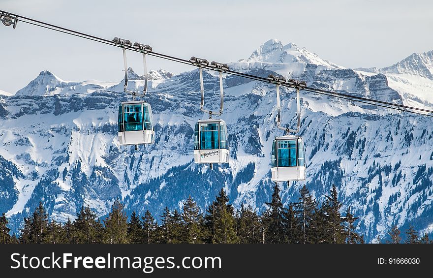 Alpine cable car over forest with snowy mountain range in background. Alpine cable car over forest with snowy mountain range in background.