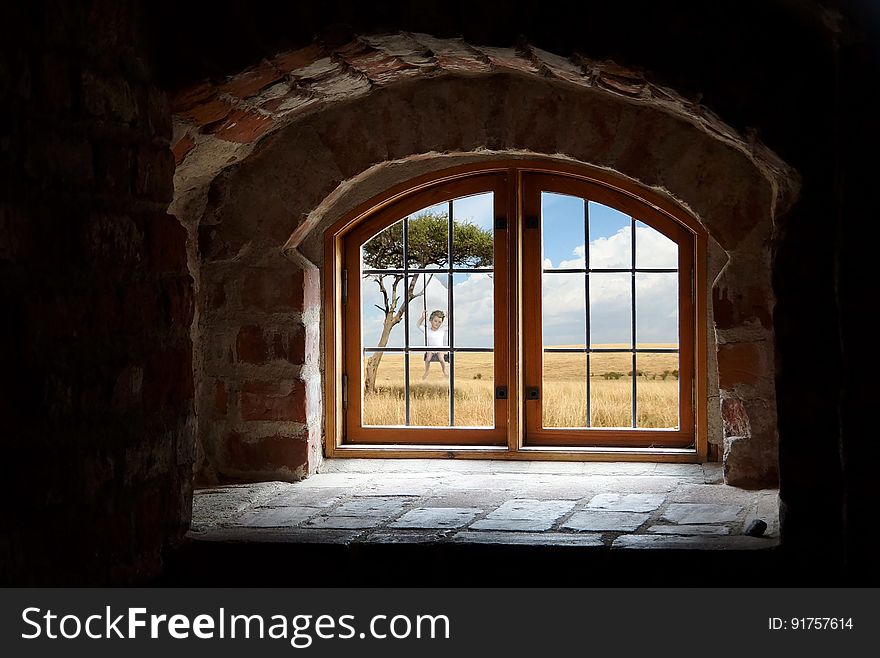 Interior view looking through window of old countryside building with child on swing under tree.