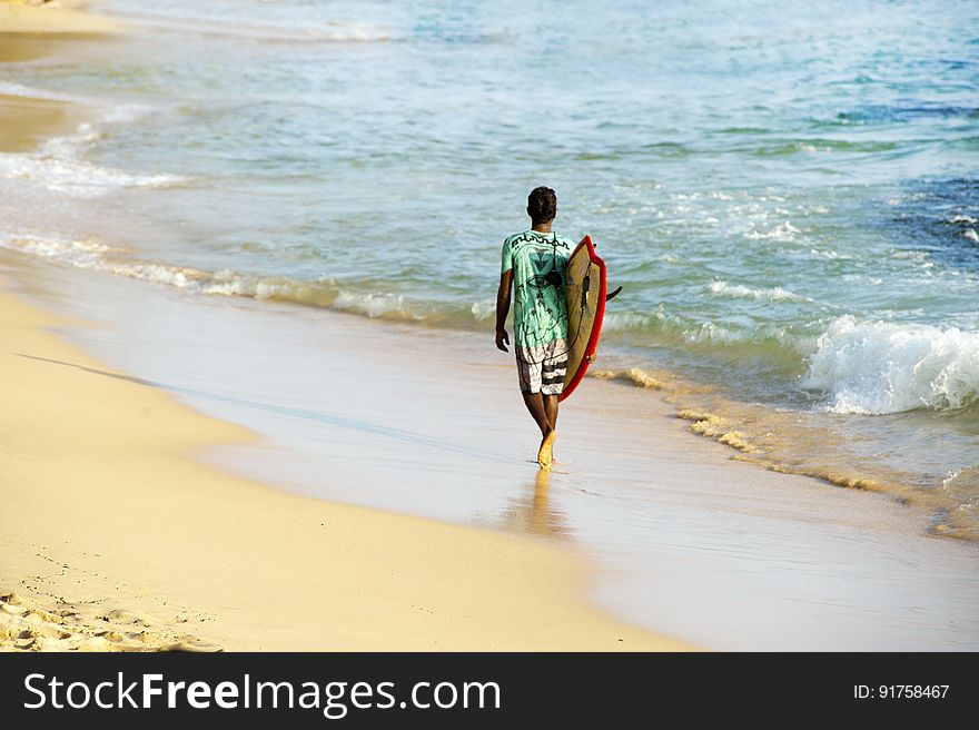 A surfer walking on a beach with his surfboard. A surfer walking on a beach with his surfboard.