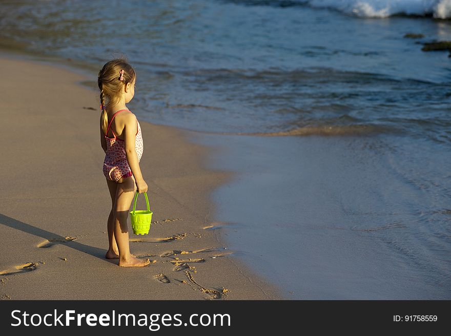 A young girl standing on the beach with a plastic pail in hand. A young girl standing on the beach with a plastic pail in hand.