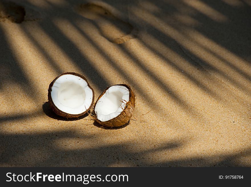 A coconut broken in two halves on a sandy beach. A coconut broken in two halves on a sandy beach.