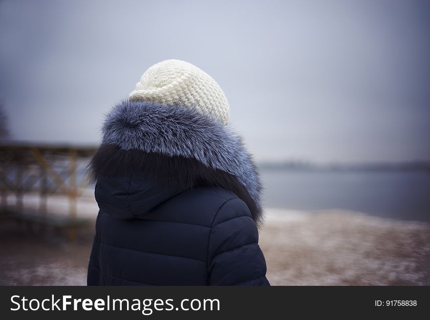 A woman wearing a beanie and a jacket wit fur-rimmed hood standing on the beach in the winter. A woman wearing a beanie and a jacket wit fur-rimmed hood standing on the beach in the winter.