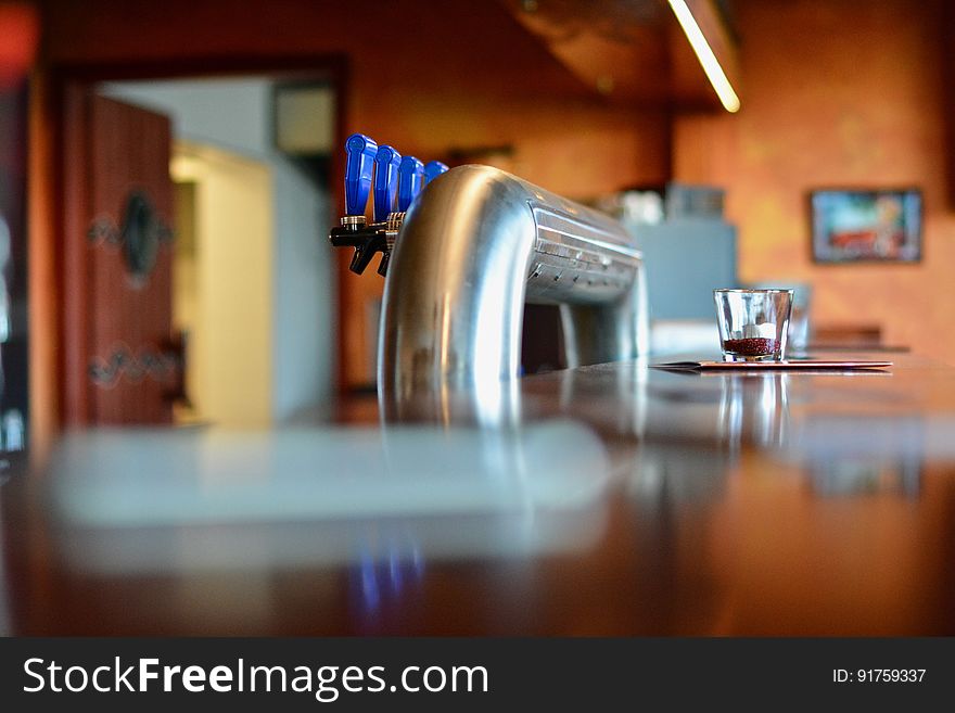 Low angle view of drinks dispenser taps in modern restaurant with wooden counter in foreground. Low angle view of drinks dispenser taps in modern restaurant with wooden counter in foreground.