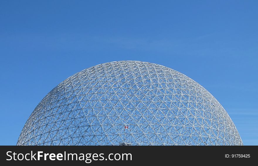 Exterior of futuristic domed glass building with blue sky background.