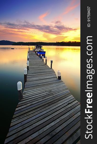 Boat moored at end of long wooden jetty on lake at sunset. Boat moored at end of long wooden jetty on lake at sunset.