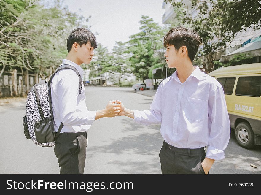 A pair of Asian men shaking hands on the street.