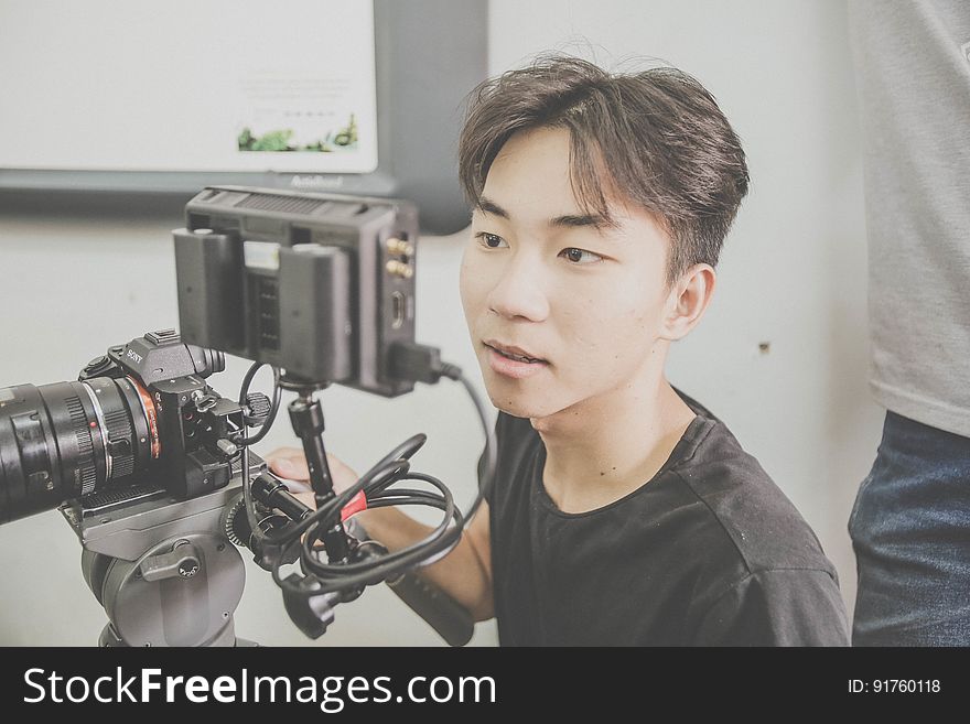 An asian man looking at an external viewfinder on a DSLR camera. An asian man looking at an external viewfinder on a DSLR camera.
