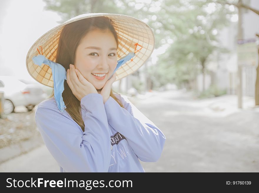 A blushing Asian woman wearing the traditional rice hat on the street. A blushing Asian woman wearing the traditional rice hat on the street.