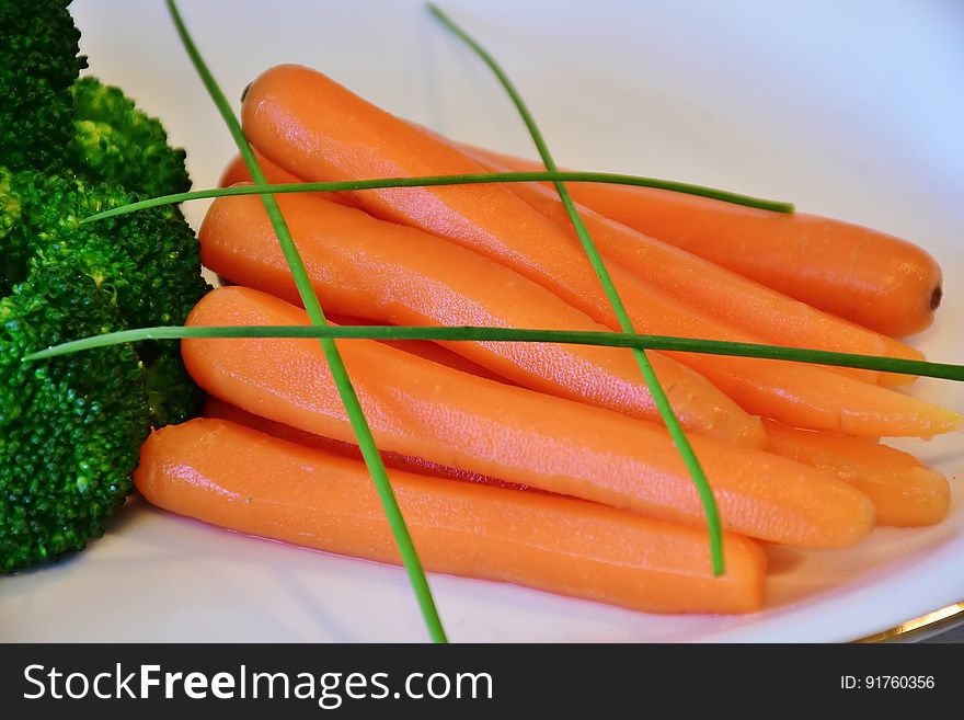 A plate with blanched carrots and broccoli with chives on top.