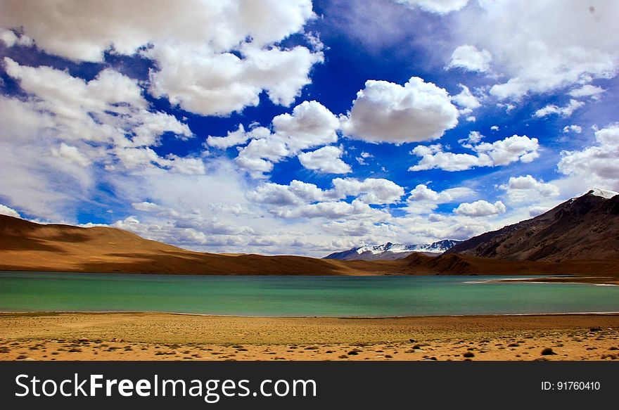 A blue sky with white clouds over a green lake and mountain range. A blue sky with white clouds over a green lake and mountain range.