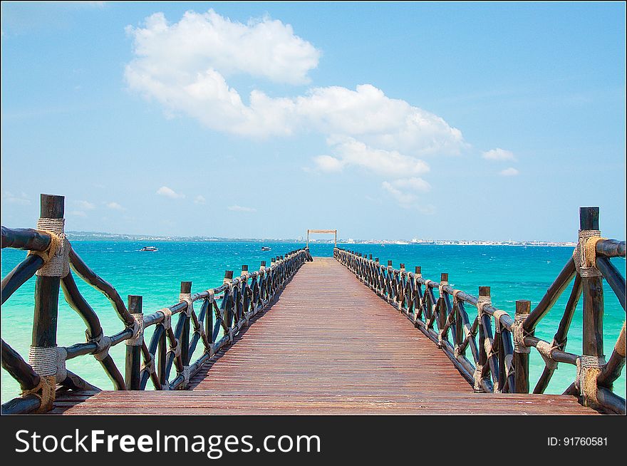 Long wooden jetty with decorative railings to left and right poking out into an aquamarine sea, pale blue sky with light clouds. Long wooden jetty with decorative railings to left and right poking out into an aquamarine sea, pale blue sky with light clouds.
