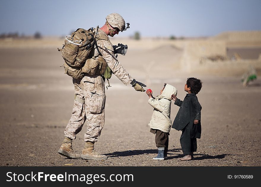 Soldier Giving Red Fruit on 2 Children during Daytime