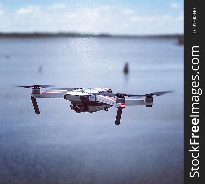 A close up a quadcopter with a camera flying over water. A close up a quadcopter with a camera flying over water.