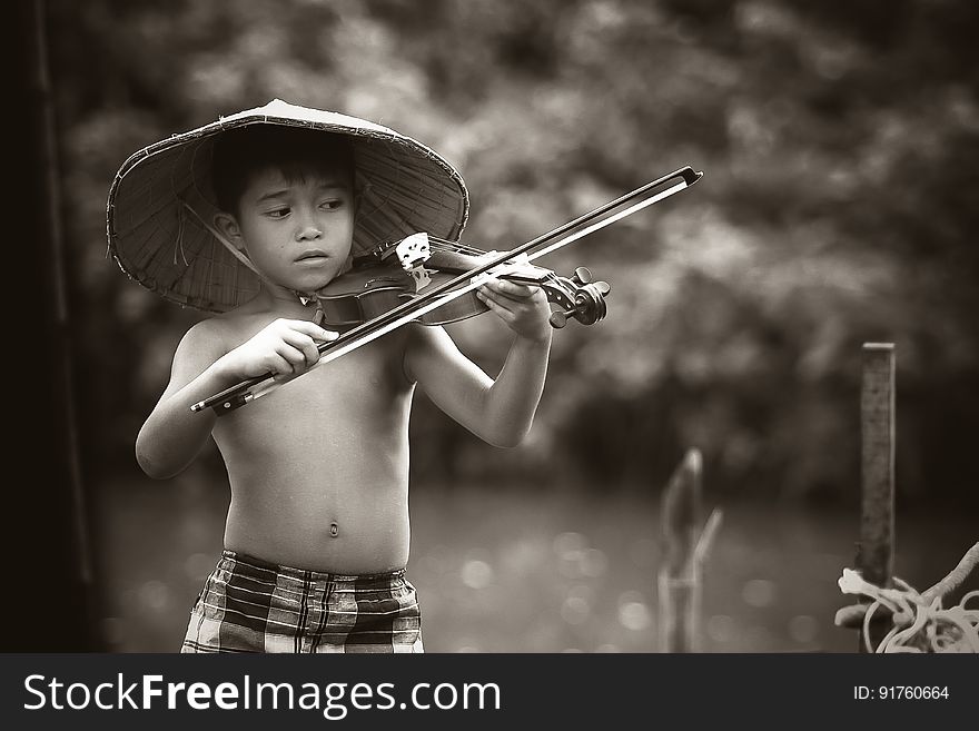 An young Asian boy wearing a traditional hat playing a violin in black and white. An young Asian boy wearing a traditional hat playing a violin in black and white.