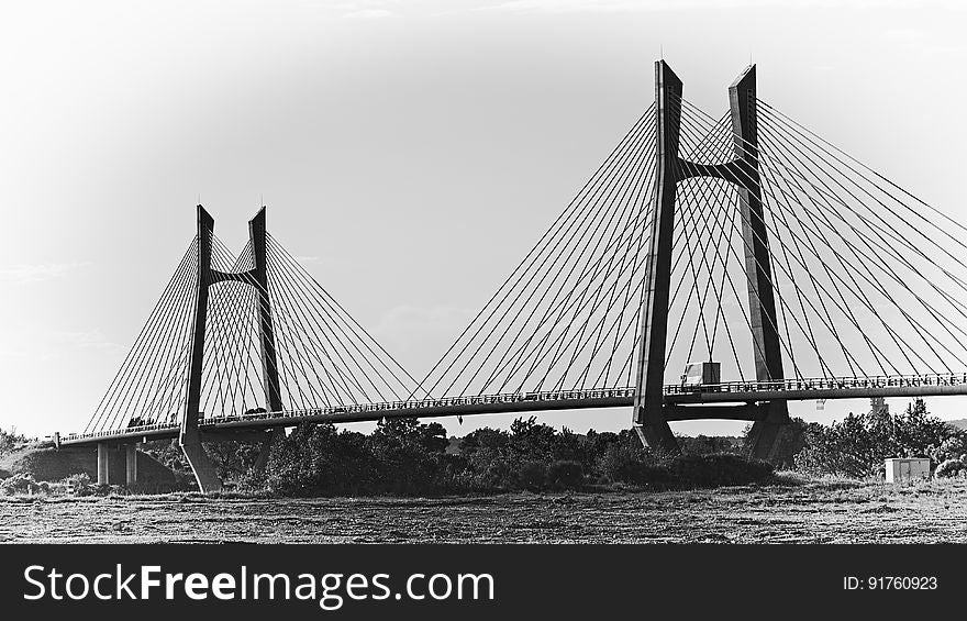 Suspension bridge across a river showing supporting cables and two towers, urban conurbation and trees are seen in silhouette..