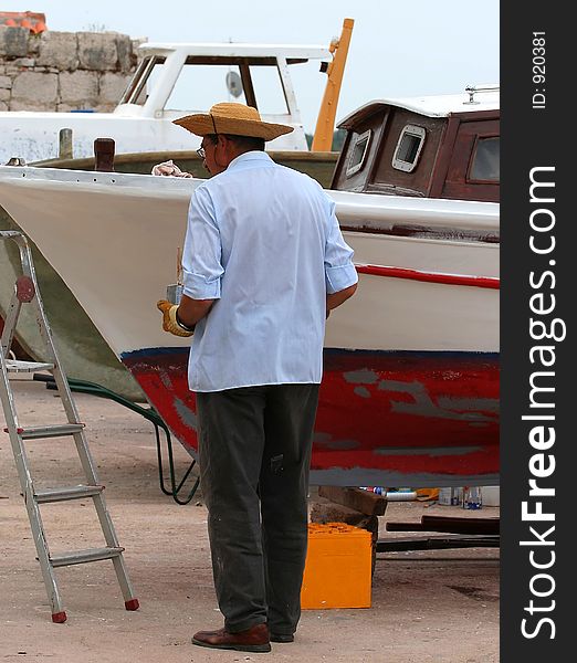 Man with hat paints the boat. Man with hat paints the boat.