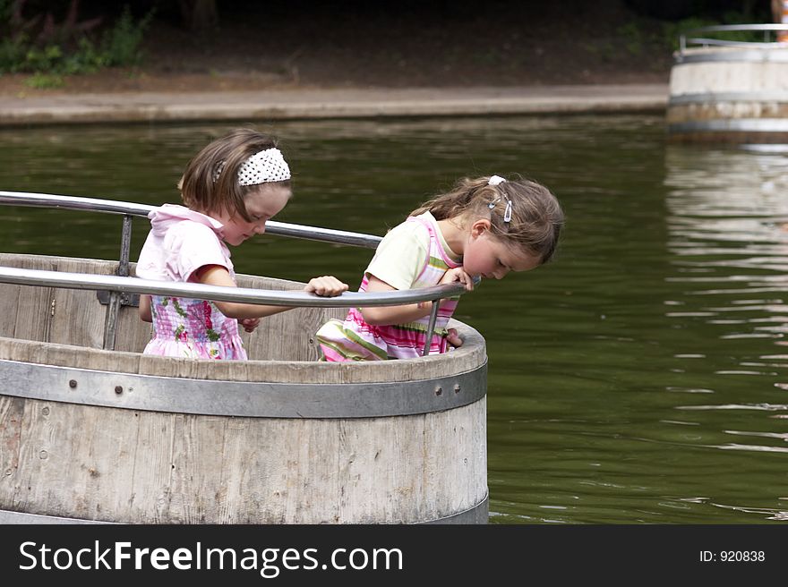 Twins playing on a playground, making a boat trip on the water in a barrel. Twins playing on a playground, making a boat trip on the water in a barrel