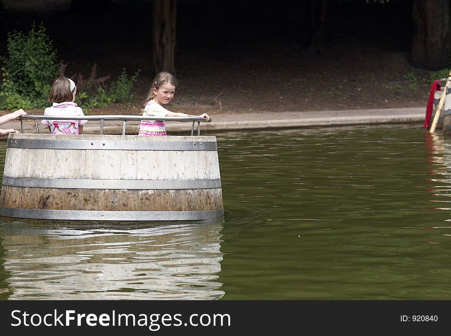 Twins playing on a playground, making a boat trip on the water in a barrel. Twins playing on a playground, making a boat trip on the water in a barrel