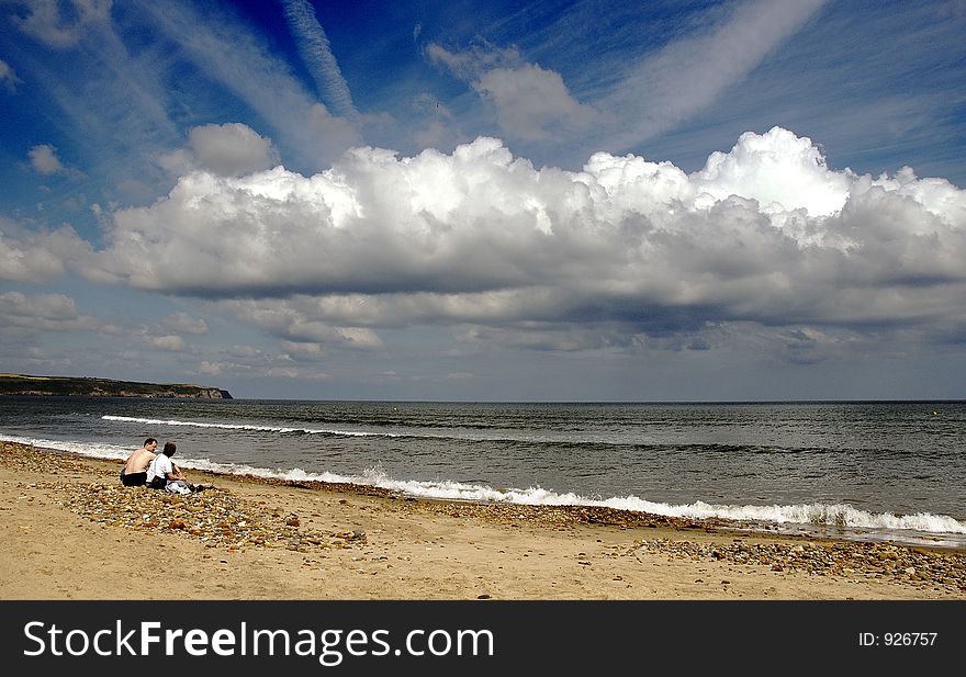 Two people sat on a beach on a bright day witha dramatic cloud. Two people sat on a beach on a bright day witha dramatic cloud.