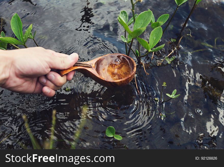 Hand Holding Wooden Ladle Extracting Water From Stream