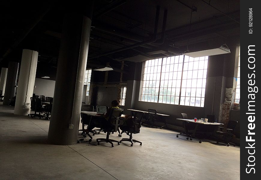 Person Sitting At Office Desk In Warehouse By Pillar