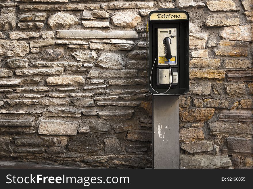 Gray And Black Telephone Booth Standing Near Gray Stone Wall At Daytime