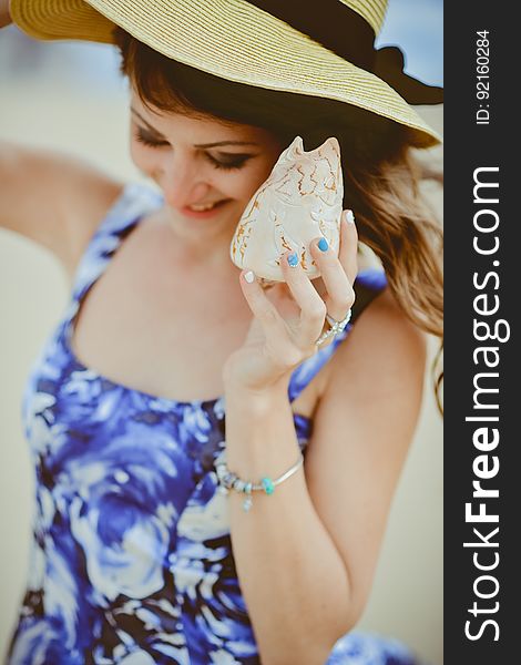 A young woman at the beach listening to a shell.