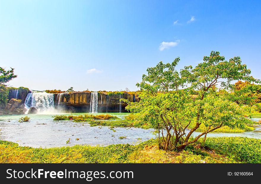 Scenic view of waterfall in green countryside with trees in foreground. Scenic view of waterfall in green countryside with trees in foreground.