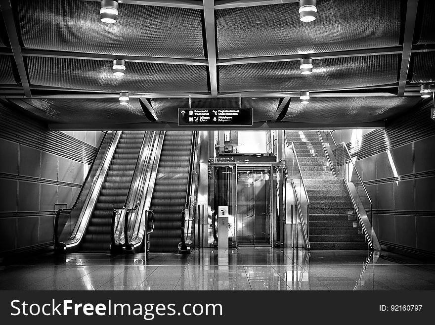 A transit hub or terminal with escalators and stairs in black and white.