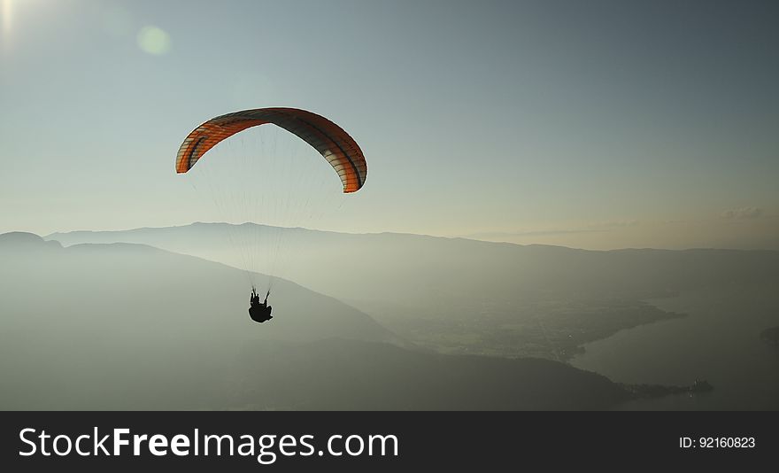 A parachutist sailing in the air over mountains and water. A parachutist sailing in the air over mountains and water.