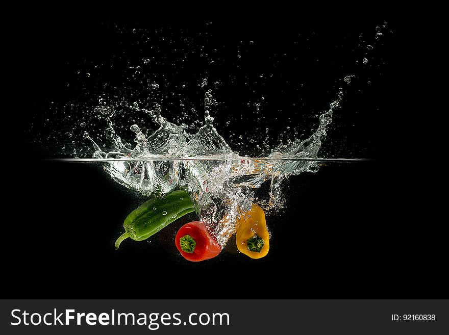 A trio of colorful peppers falling in water on black background. A trio of colorful peppers falling in water on black background.
