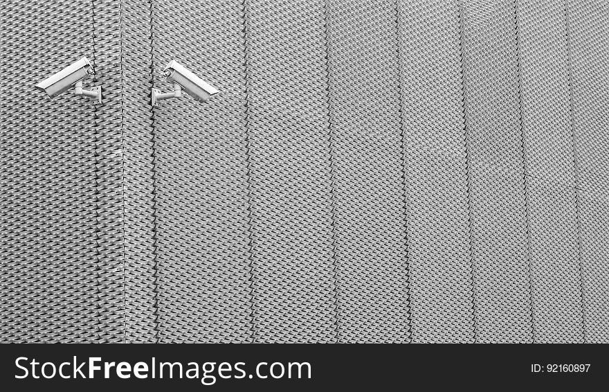Security surveillance cameras on exterior aluminum fence in daylight. Security surveillance cameras on exterior aluminum fence in daylight.