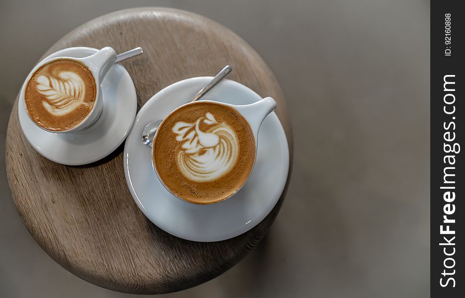 Overhead view of cups with coffee latte on saucers with spoons on wooden board. Overhead view of cups with coffee latte on saucers with spoons on wooden board.