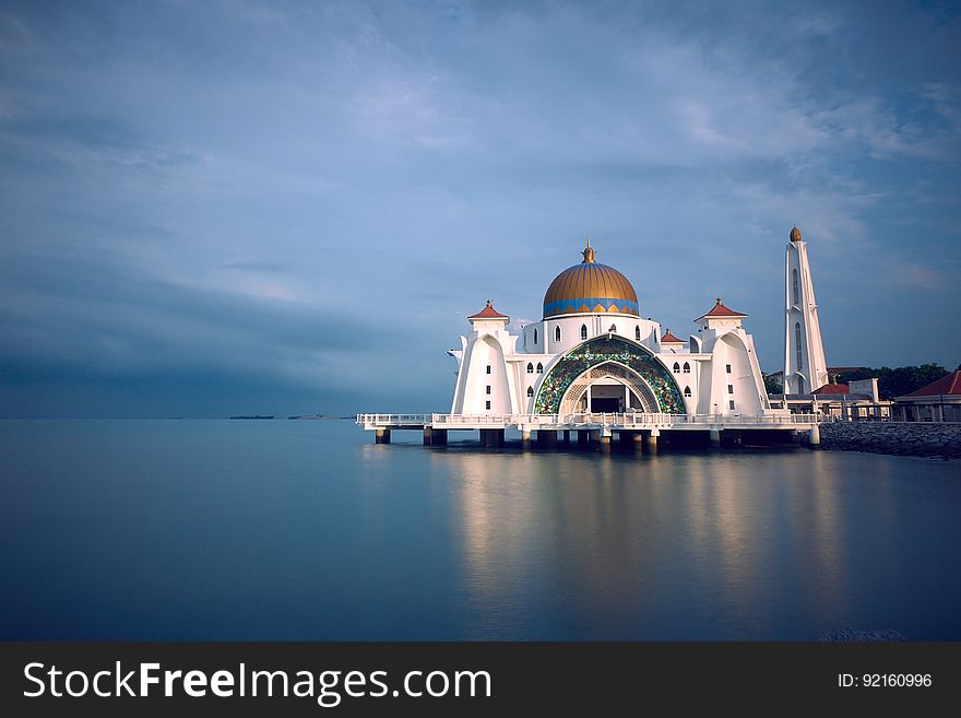 Gold domed white mosque on waterfront of Malaysia against blue skies on cloudy day. Gold domed white mosque on waterfront of Malaysia against blue skies on cloudy day.