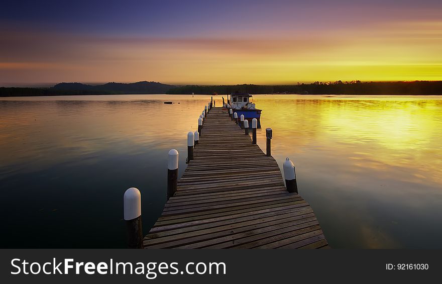 Empty wooden dock leading to clear river at sunset. Empty wooden dock leading to clear river at sunset.