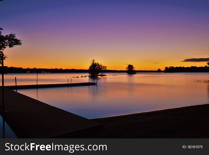 Sunset over river waterfront with silhouette of trees.