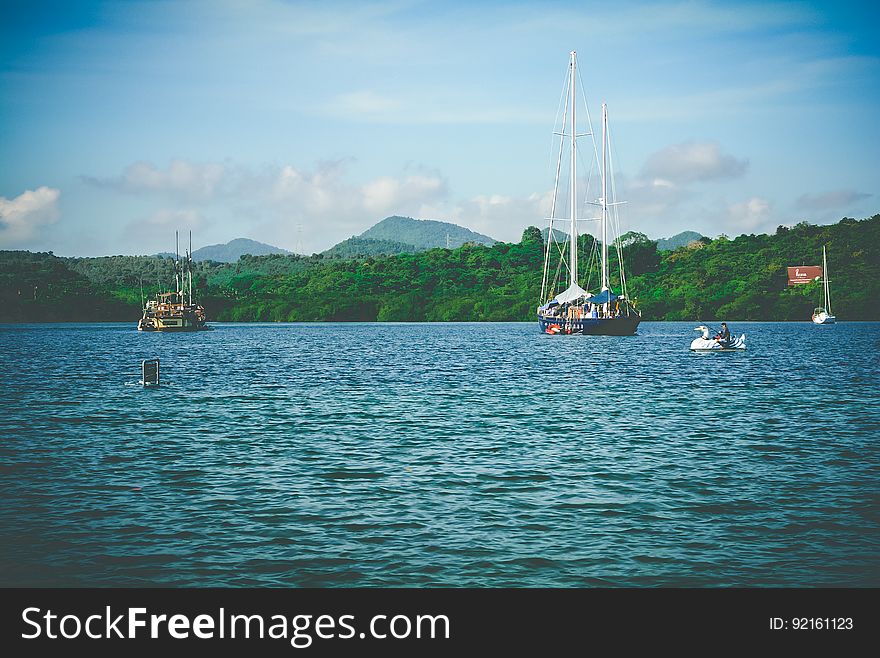 A summer scene with sailboats and paddleboats in the water. A summer scene with sailboats and paddleboats in the water.