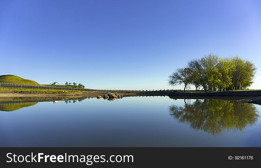 Rural landscape with reflection on tree on banks of clear blue waters on sunny day. Rural landscape with reflection on tree on banks of clear blue waters on sunny day.