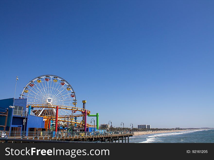Seaside carnival with rides and Ferris Wheel on sunny day against blue skies. Seaside carnival with rides and Ferris Wheel on sunny day against blue skies.