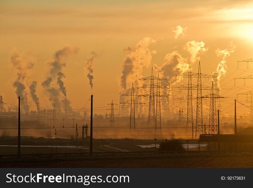 Industrial smokestacks with plumes of steam or pollution with electrical stanchions at sunset. Industrial smokestacks with plumes of steam or pollution with electrical stanchions at sunset.
