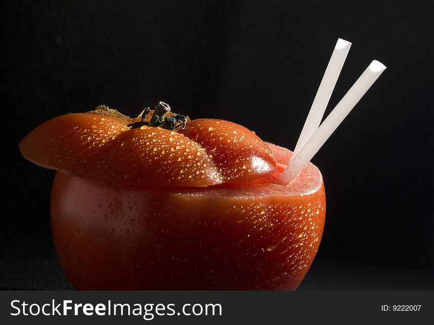 Ripe red tomato covered in clear morning dew drops. Freshly picked from the garden and sliced with two straws inserted in it. Ripe red tomato covered in clear morning dew drops. Freshly picked from the garden and sliced with two straws inserted in it.