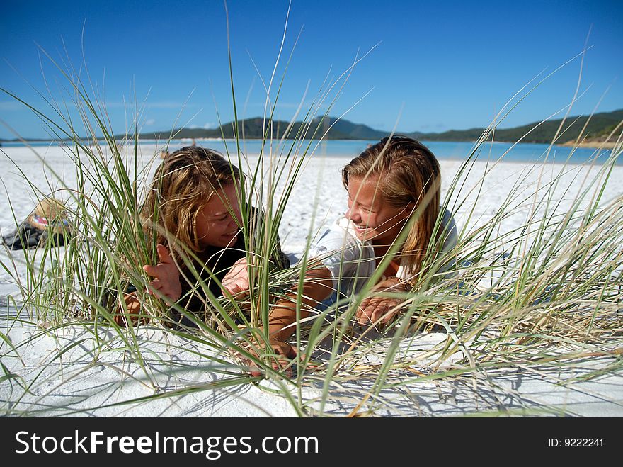 Two beautiful young women hiding behind grass on the beach in the sand at beach. Two beautiful young women hiding behind grass on the beach in the sand at beach