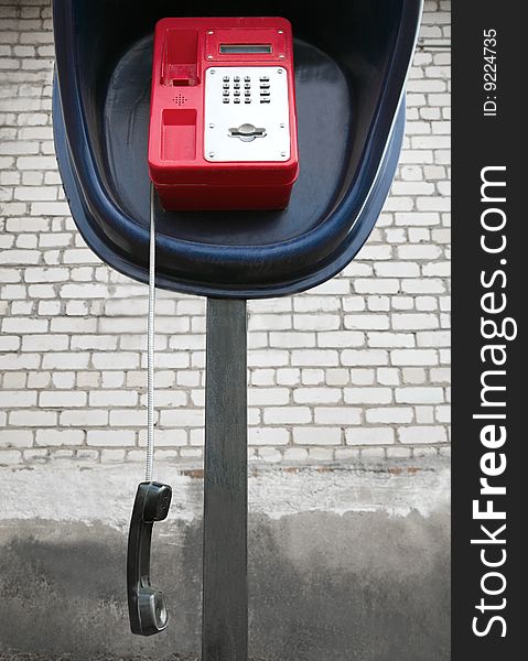 The red payphone with a hanging tube. The red payphone with a hanging tube