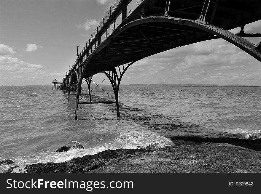 View of Clevedon Pier from shore with fluffy clouds and turbulent sea