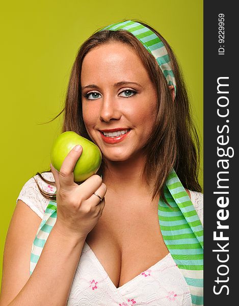 Brunette holding apple and smiling against a green background