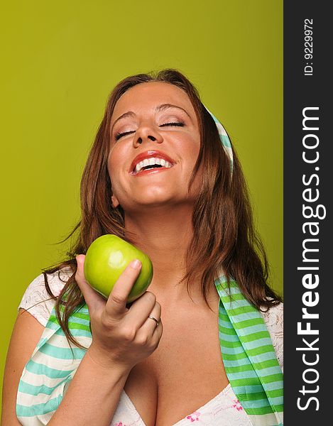 Brunette holding apple and smiling against a green background