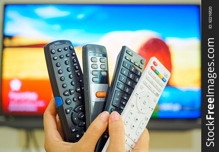 Close up Hand holding TV remote control with a television in the background.