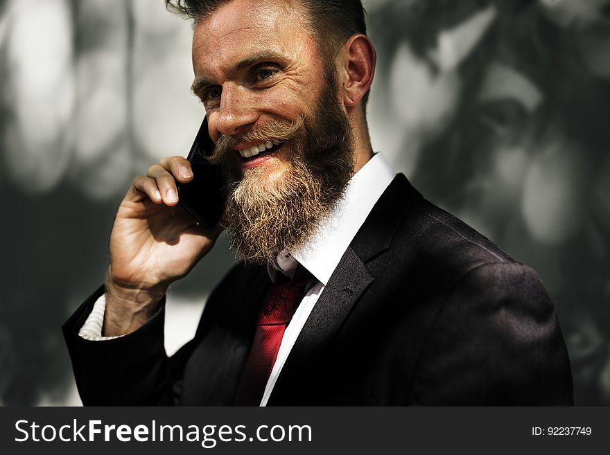 Portrait of smiling smartly dressed businessman listening (conversing) on mobile phone, blurred background. Portrait of smiling smartly dressed businessman listening (conversing) on mobile phone, blurred background.